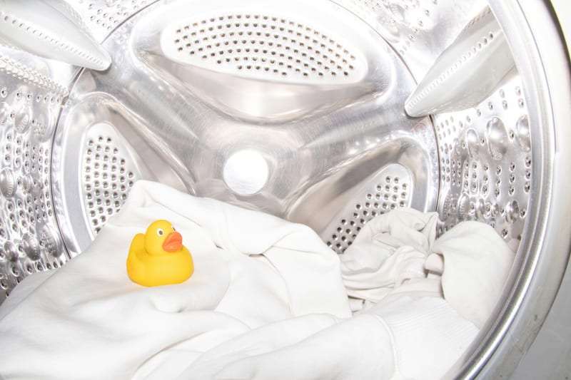 a yellow rubber duck sits on a white cloth in a washing machine