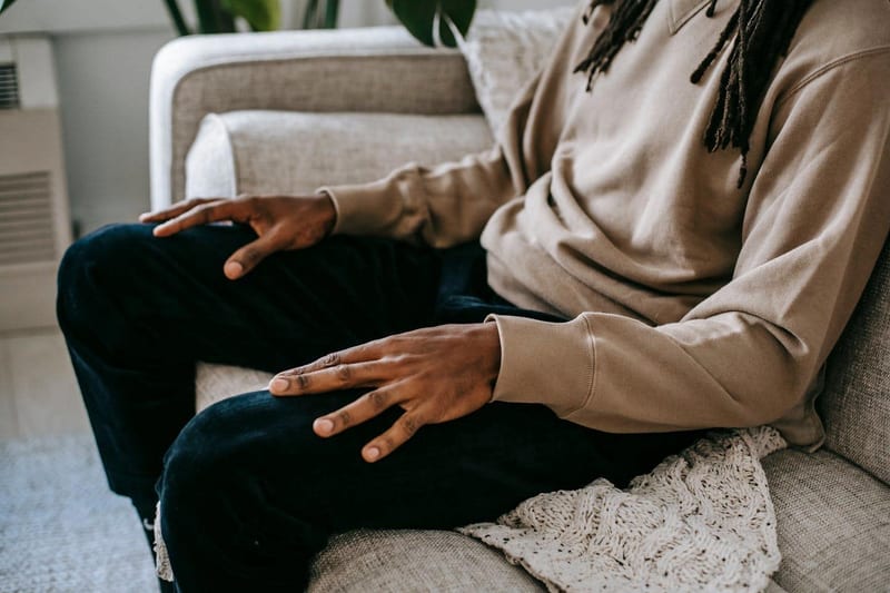 a man with dreadlocks is sitting on a couch with his hands folded