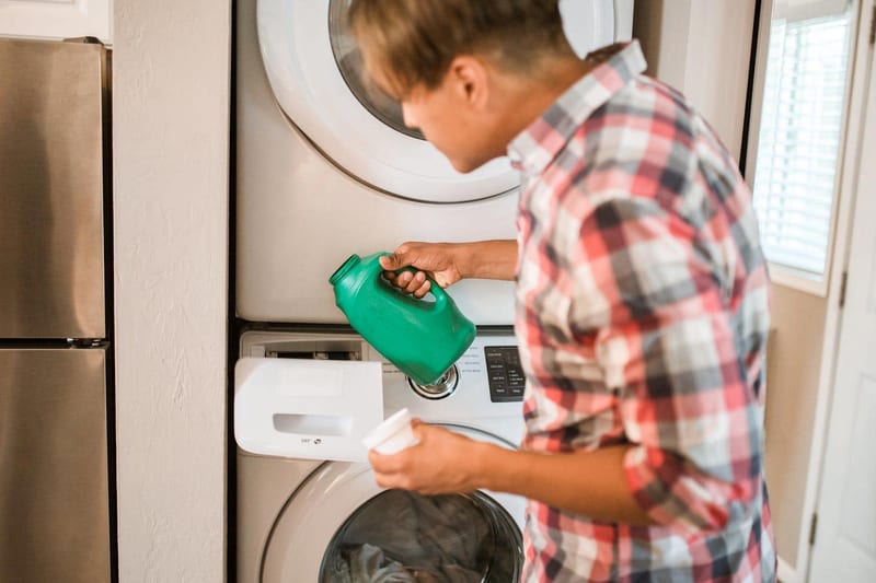 a man is pouring laundry detergent into a stacked washer and dryer