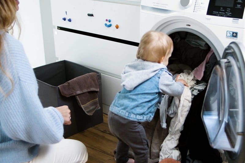 a woman and a baby are doing laundry in a washing machine