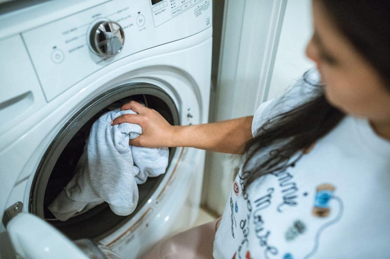 a woman is putting clothes into a washing machine