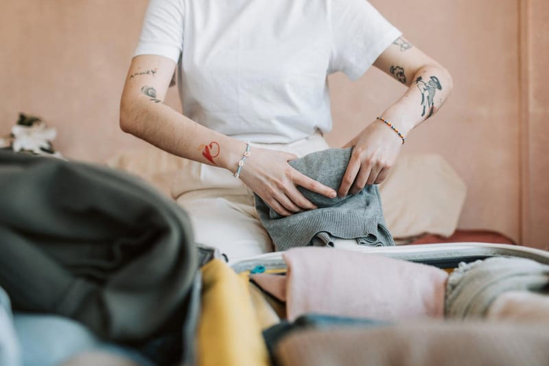 a woman is sitting on a bed packing clothes into a suitcase