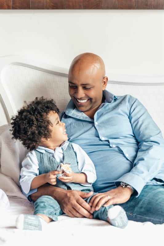 a man and a little boy are sitting on a bed and smiling
