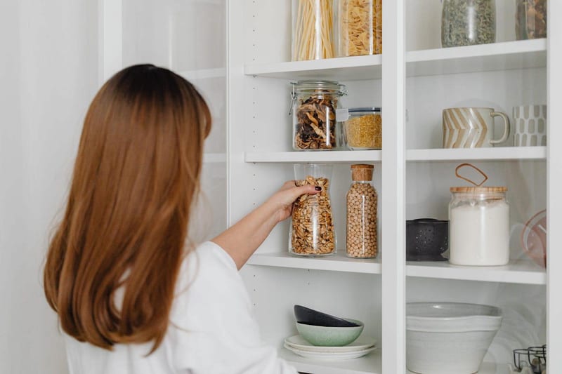 a woman is taking a jar of granola out of a pantry