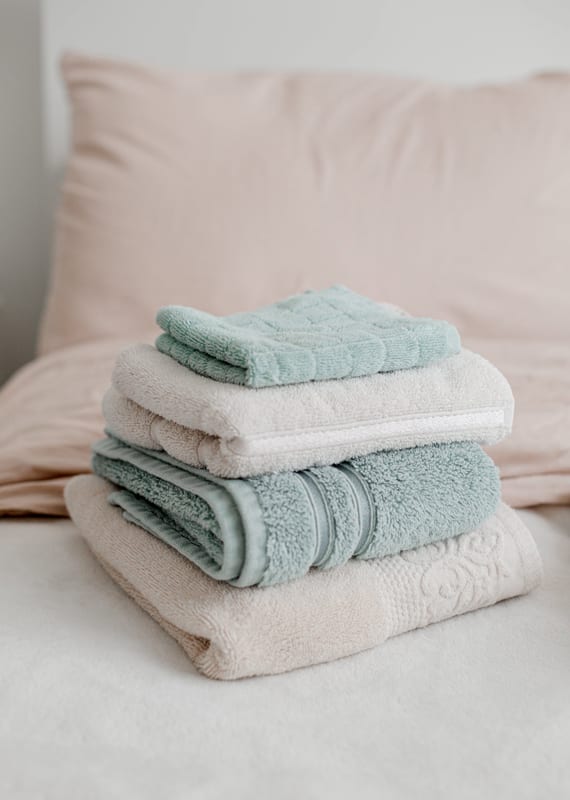 a stack of towels on a bed with a pink pillow