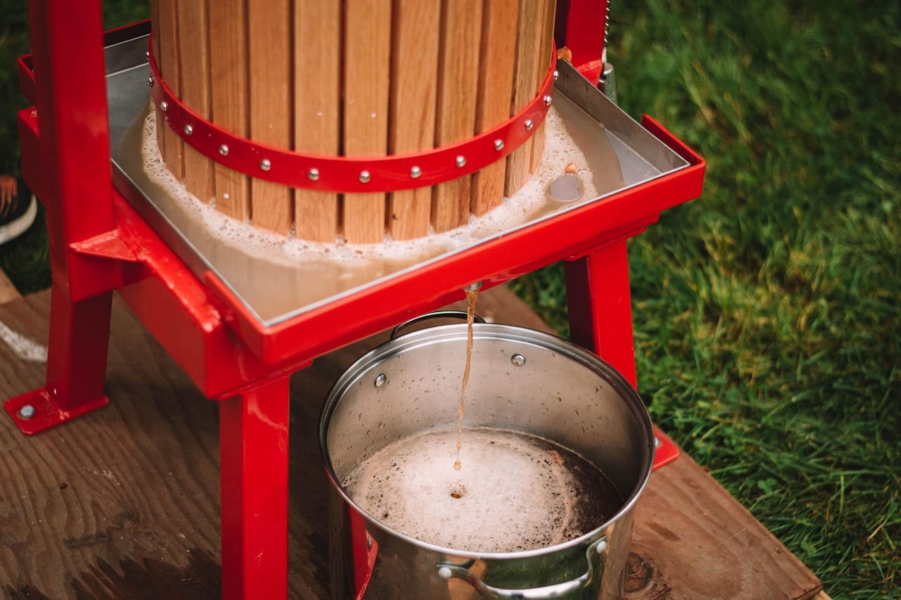 Fresh apple juice running from a wooden cider press into a steel pail