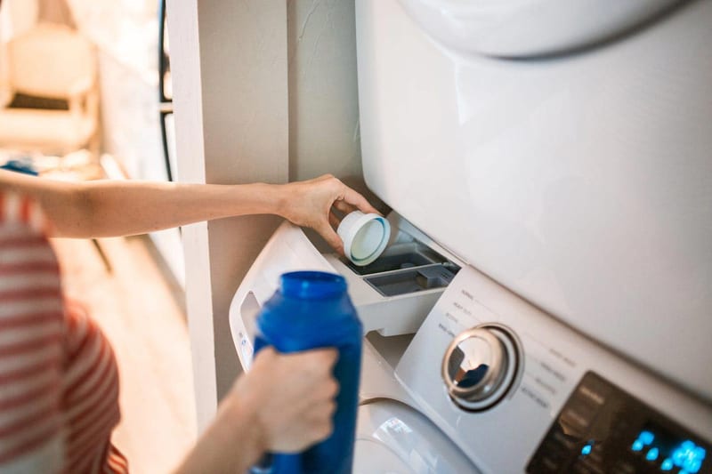 a woman is pouring detergent into a washing machine
