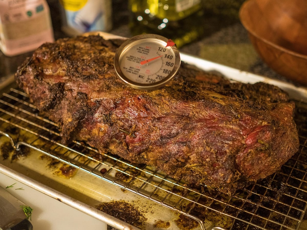 A browned beef roast on a wire rack with a dial meat thermometer in it