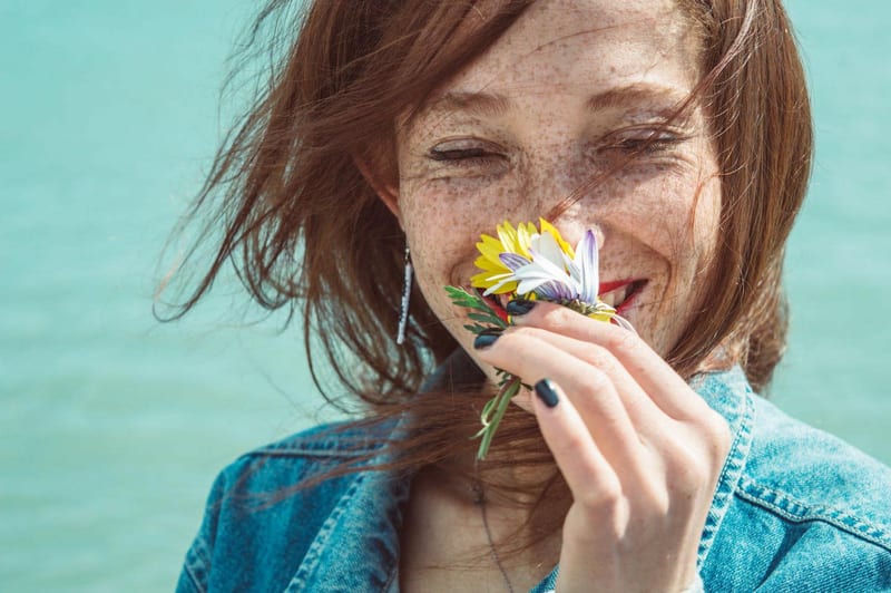 a woman with freckles is holding a flower in front of her face