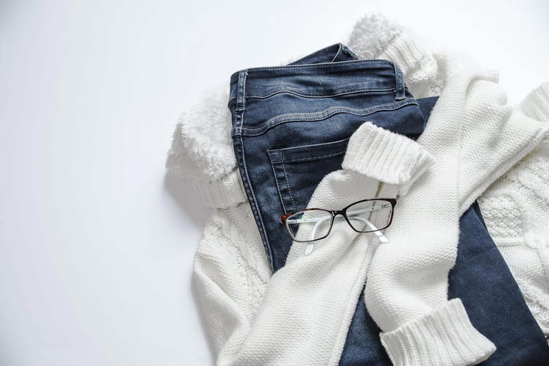 a white sweater , blue jeans , a white sweater and glasses on a white background