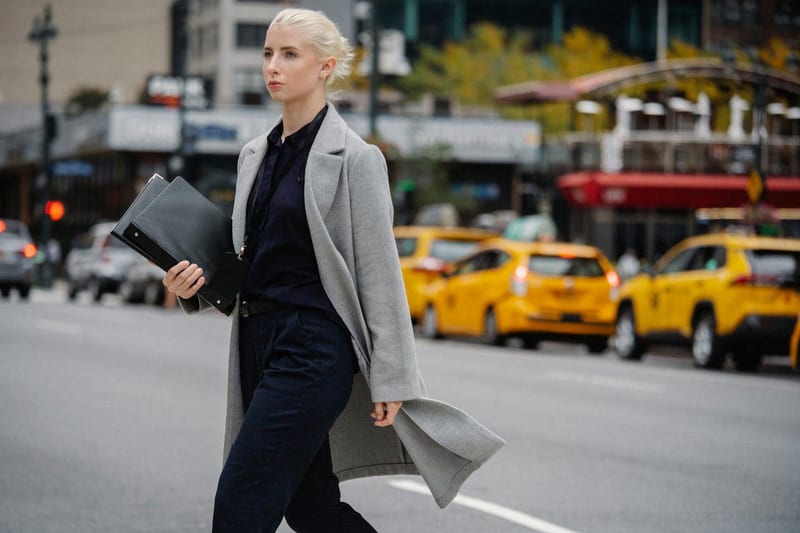 a woman in a grey coat is walking down the street