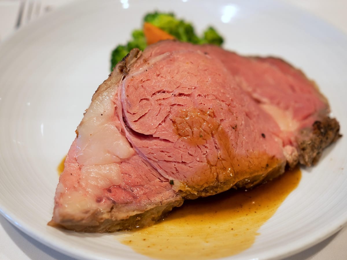 A thick slice of medium-rare prime rib on a plate with jus