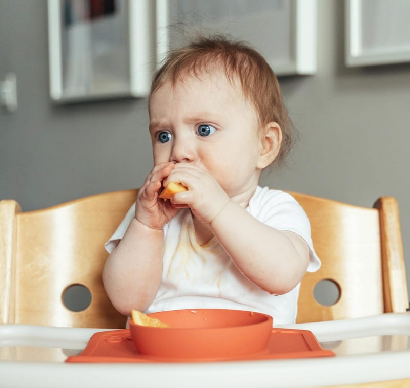 a baby is sitting in a high chair eating an orange