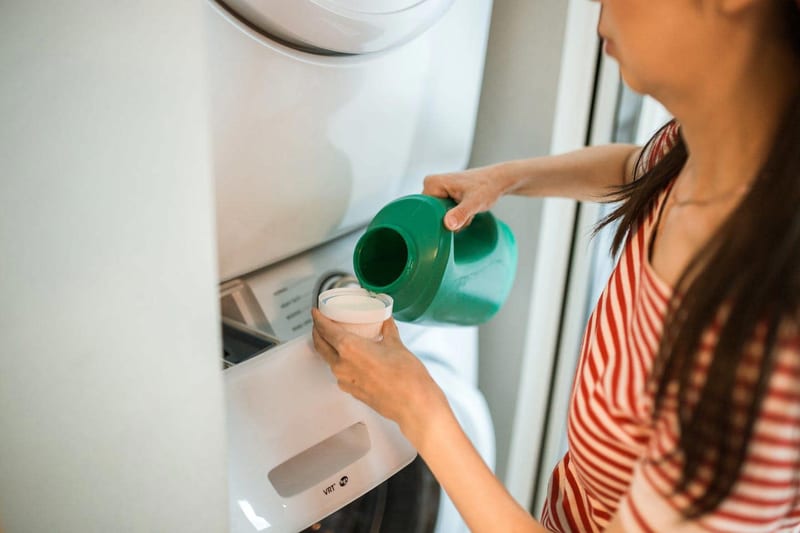 a woman is pouring laundry detergent into a washing machine