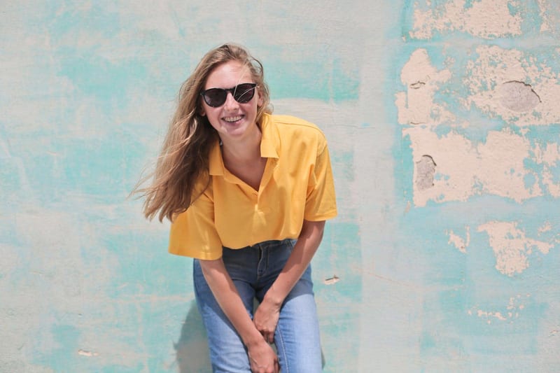 a woman wearing sunglasses and a yellow shirt is sitting in front of a blue wall
