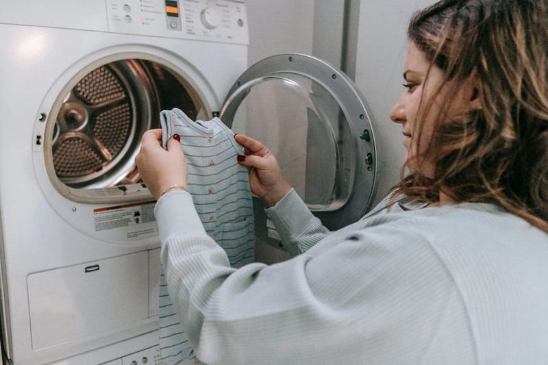a woman is putting clothes in a washing machine
