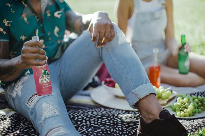 a man sits on a blanket holding a bottle of jarritos