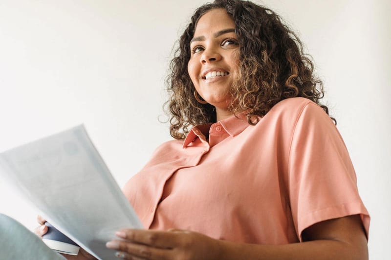 a woman in a pink shirt is holding a piece of paper and smiling