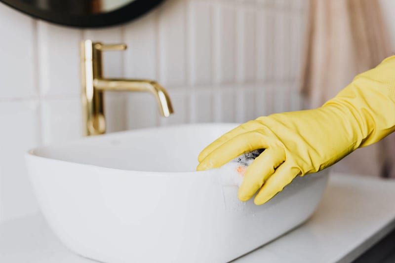a person wearing yellow gloves is cleaning a bathroom sink with a sponge
