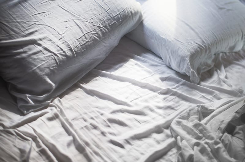 a bed with white sheets and pillows on it