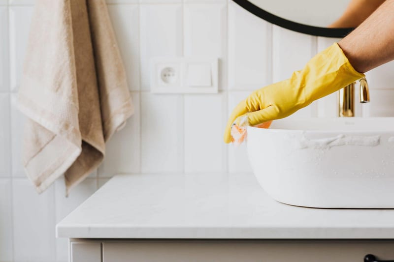 a person wearing yellow gloves is cleaning a bathroom sink