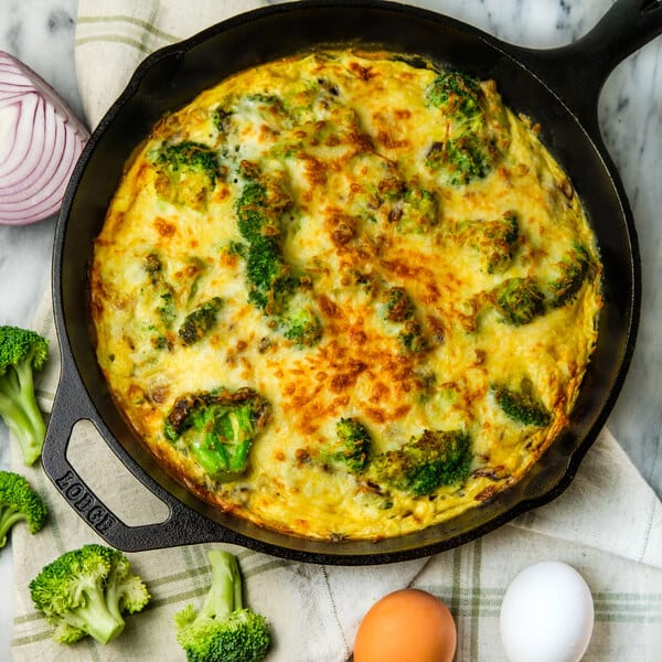 Cast iron skillet frittata with broccoli and melted cheese on a marble surface