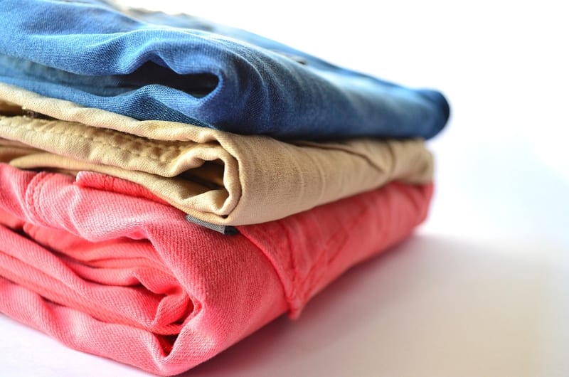 a stack of folded clothes includes a pink shirt and a blue shirt