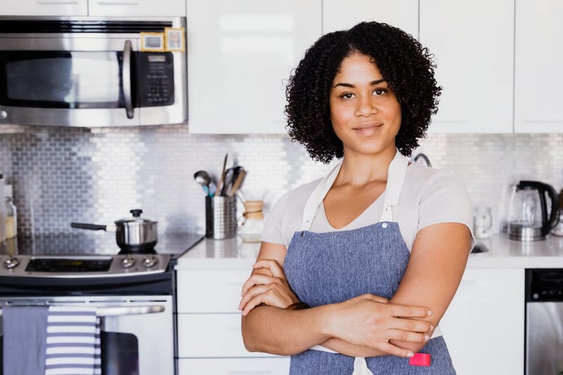 a woman in an apron stands in a kitchen with her arms crossed