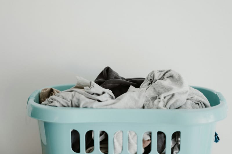a blue laundry basket filled with clothes against a white wall