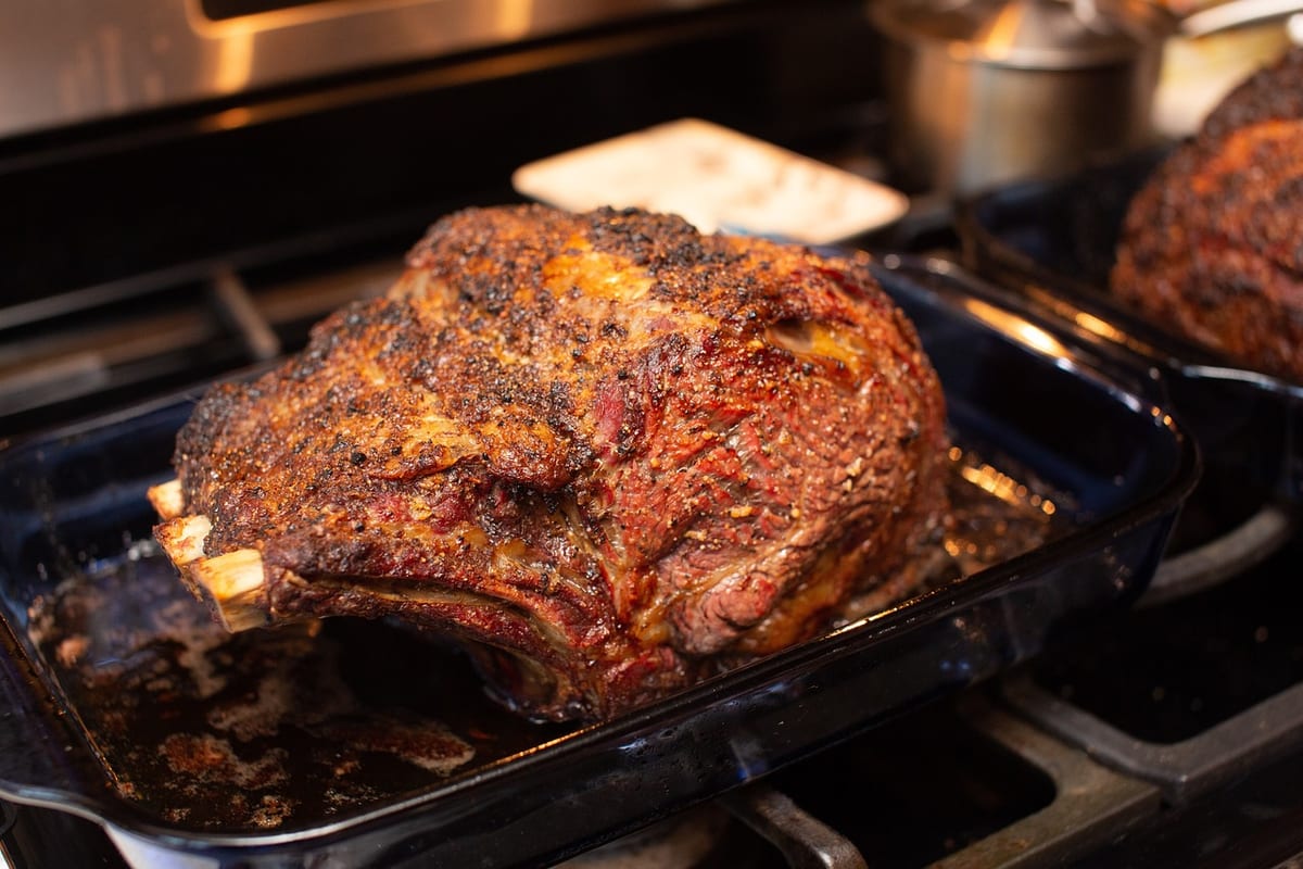 A seasoned bone-in rib roast in a roasting pan, just out of the oven