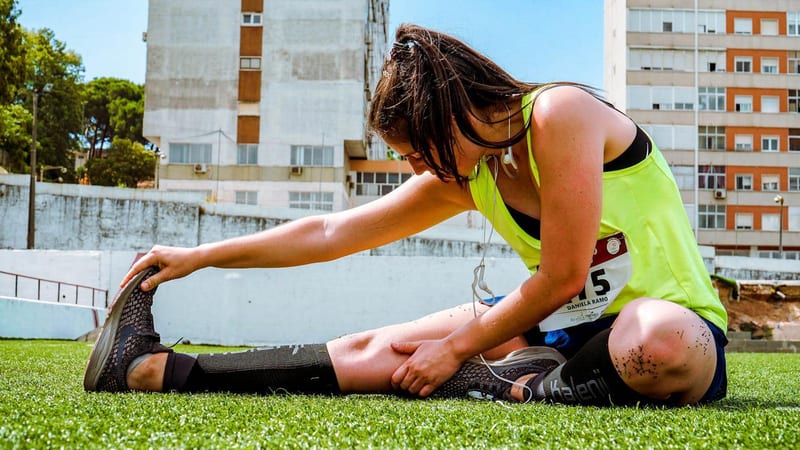 a woman wearing a yellow tank top with the number 5 on it stretches her legs