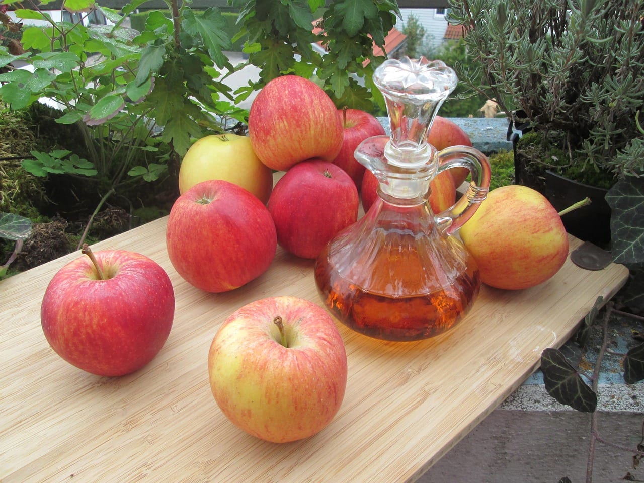 A glass cruet of apple cider vinegar next to red apples on a wooden board